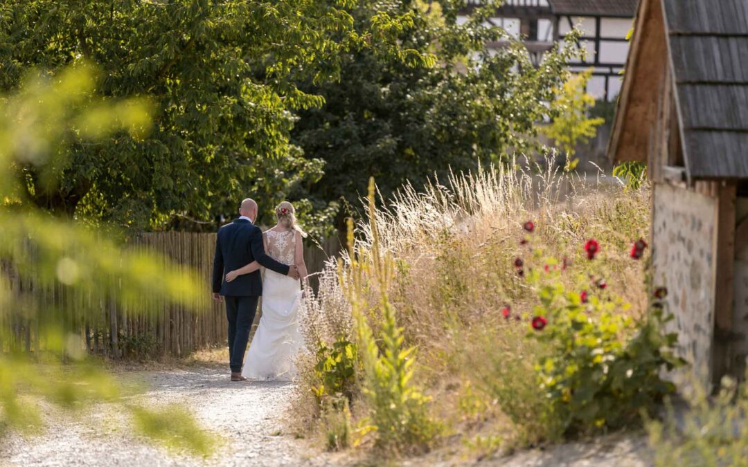 Brautpaar spaziert auf einem Gartenweg zwischen Blumen und Gräsern