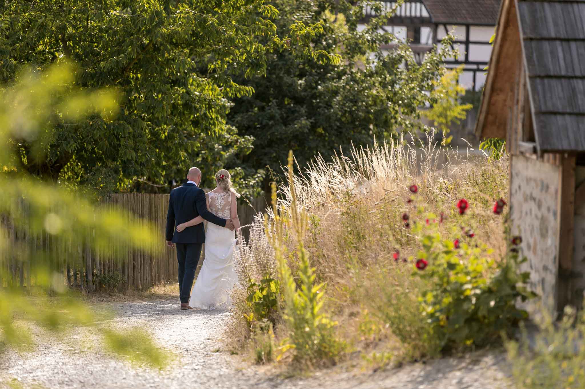 Brautpaar spaziert auf einem Gartenweg zwischen Blumen und Gräsern
