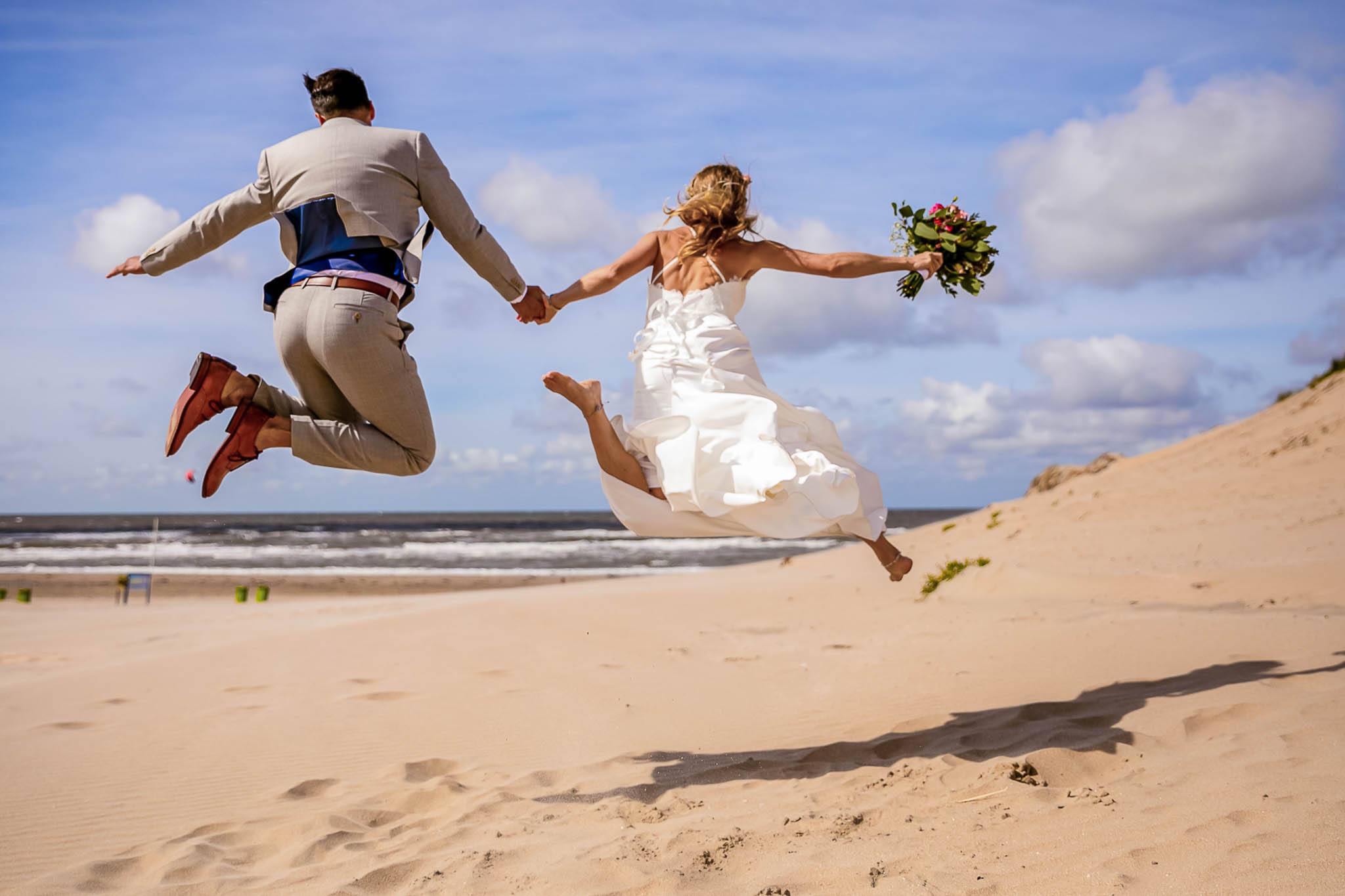 Sprung in den Dünen Brautpaar springt ausgelassen über eine Sanddüne am Meer