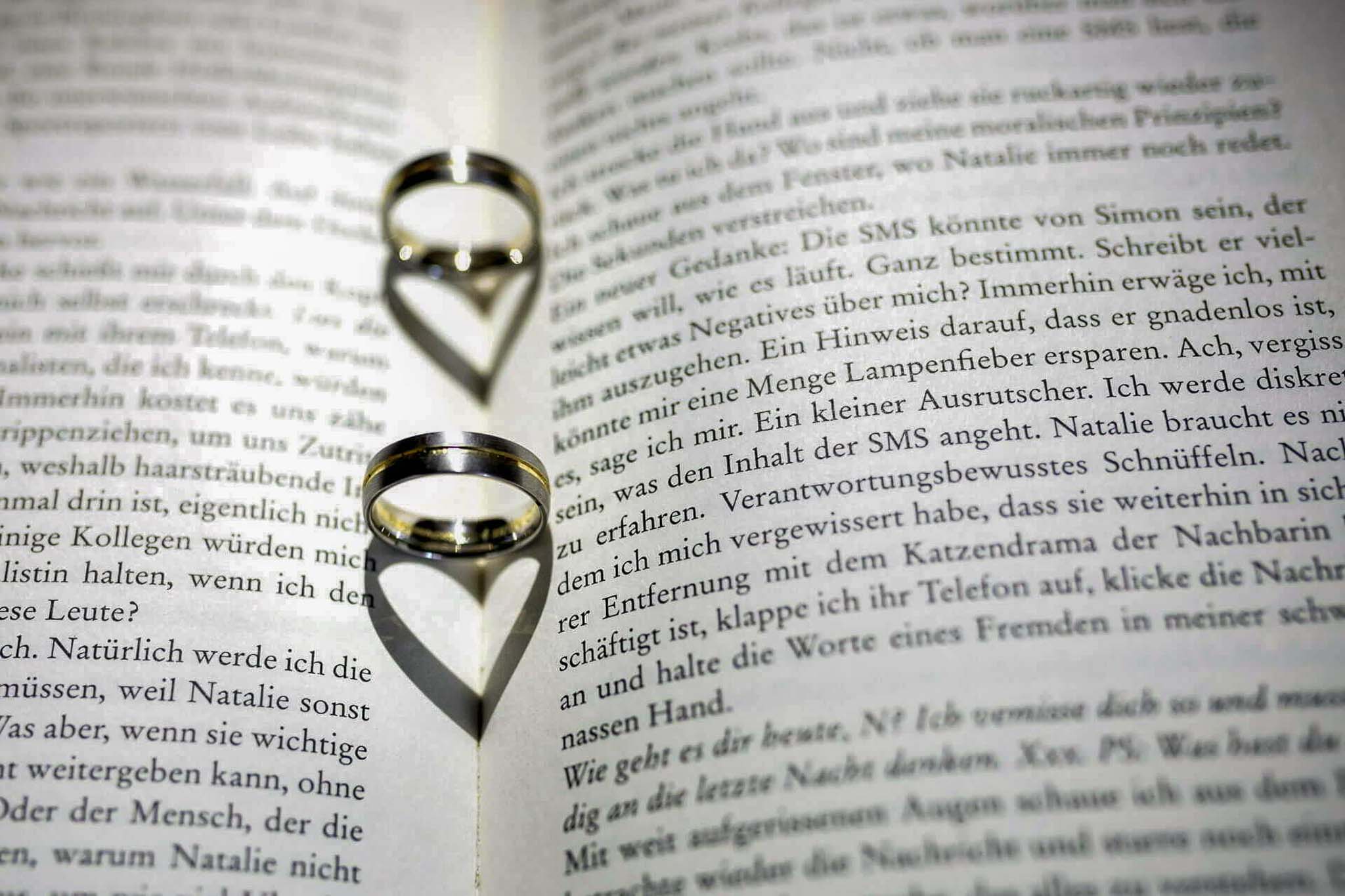 Zwei Eheringe auf einem aufgeschlagenen Buch werfen ein Herz als Schatten