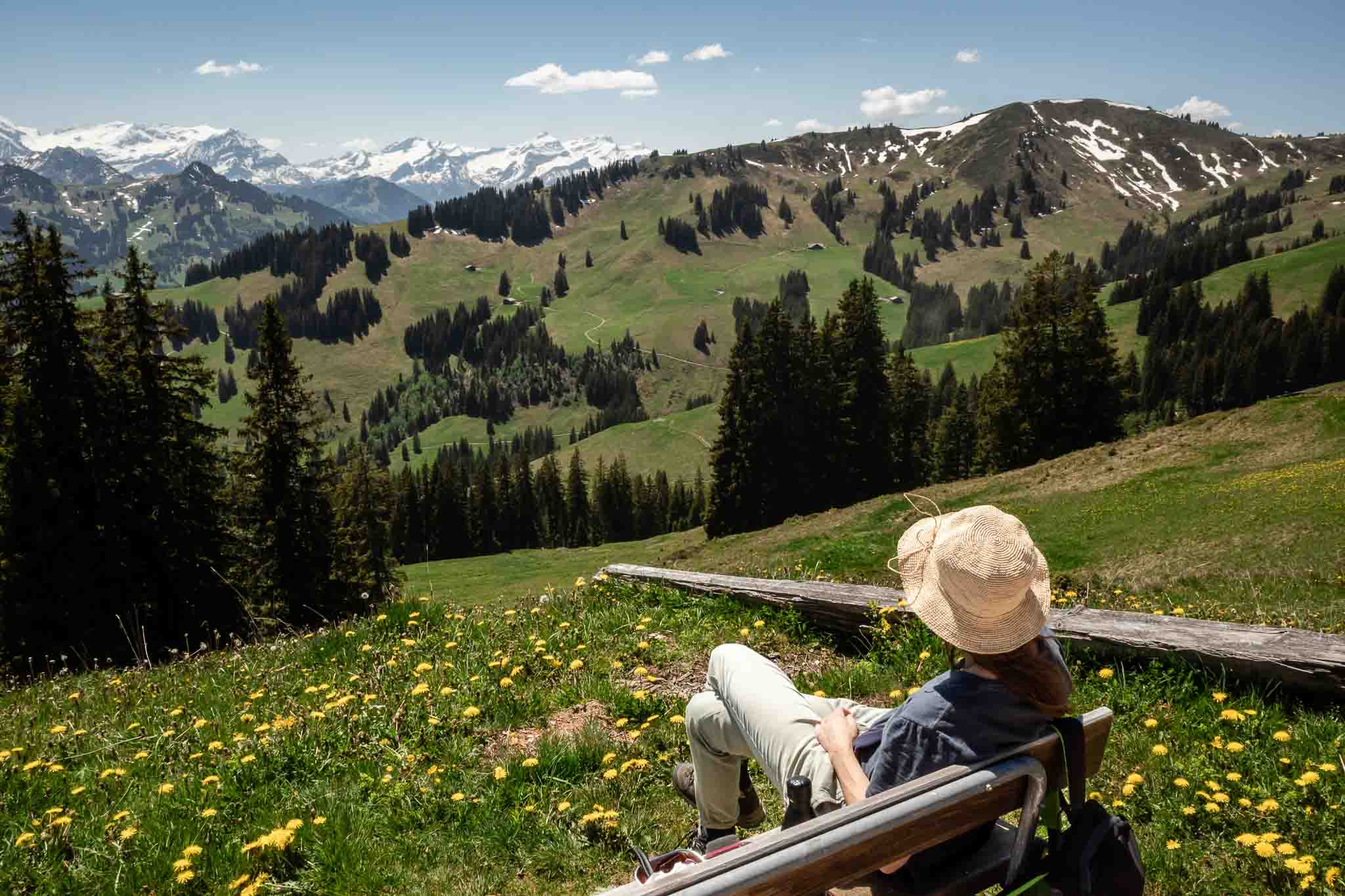 Person mit Hut ruht auf einer Bank auf einer Alpwiese vor Schweizer Bergen